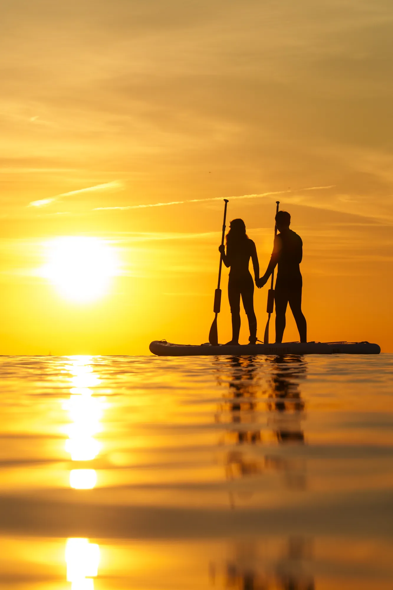 Couple en paddle au coucher du soleil à Sitges, lumière dorée sur la mer face à Terramar