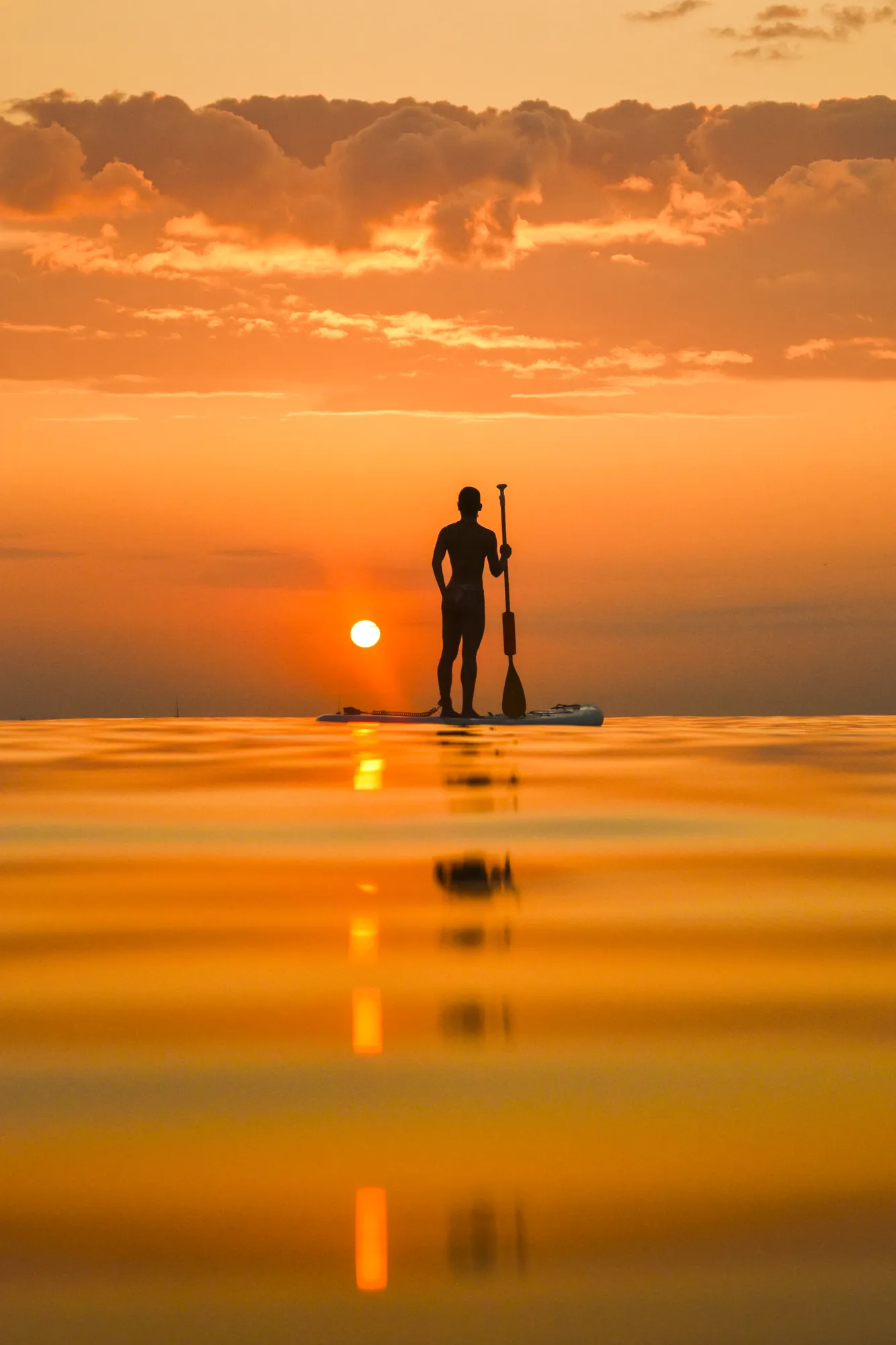 Homme en stand up paddle au lever du soleil à Sitges, mer d'huile sur la Platja de la Riera Xica