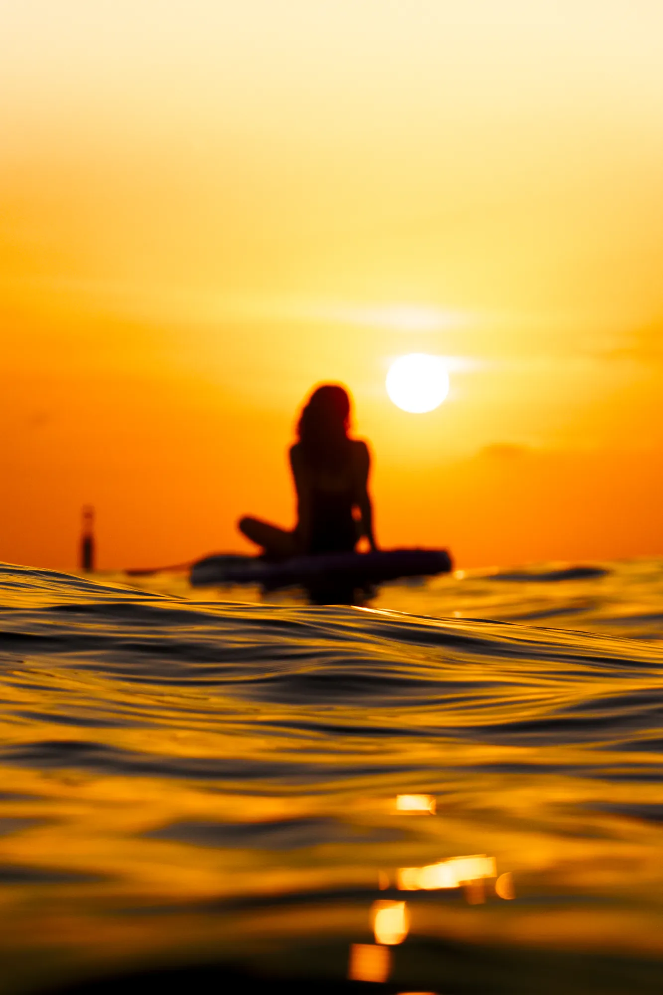Femme sur une planche de paddle au lever du soleil à Sitges, vue au ras de l'eau